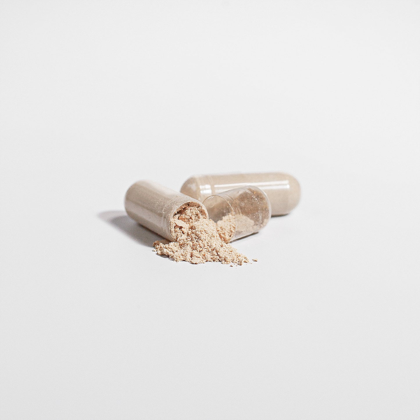 Close-up of Brainwave Organics Lion's Mane Mushroom Supplement capsules. Beige capsules with one open to reveal finely ground mushroom powder, displayed on a clean white background.